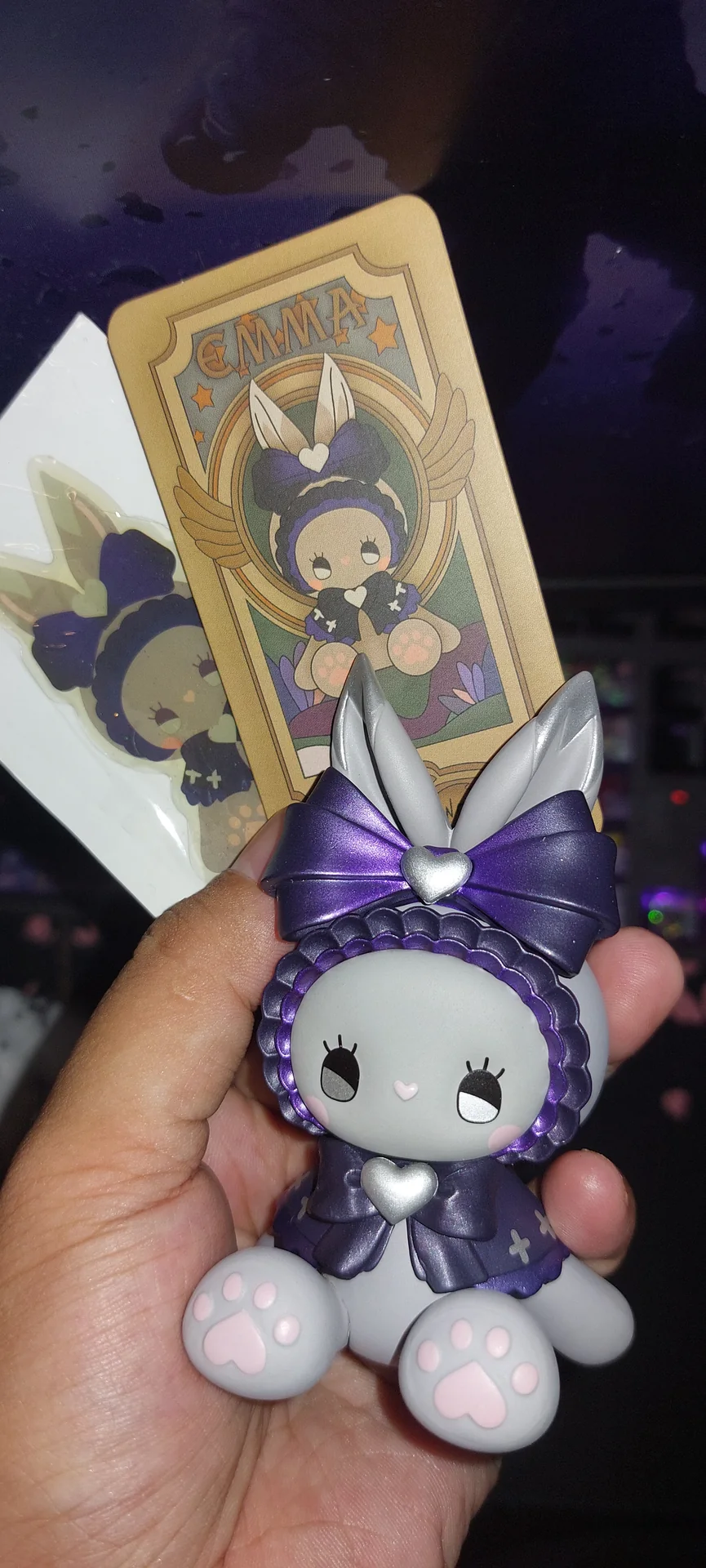 A purple bunny-eared collectible figure named Emmya held up beside its matching art card