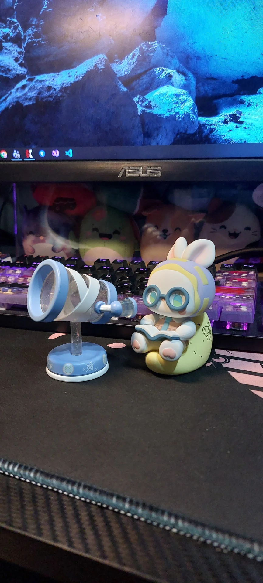 A bunny-eared figure with glasses reading a book while perched on a crescent moon, beside a small toy telescope on the desk