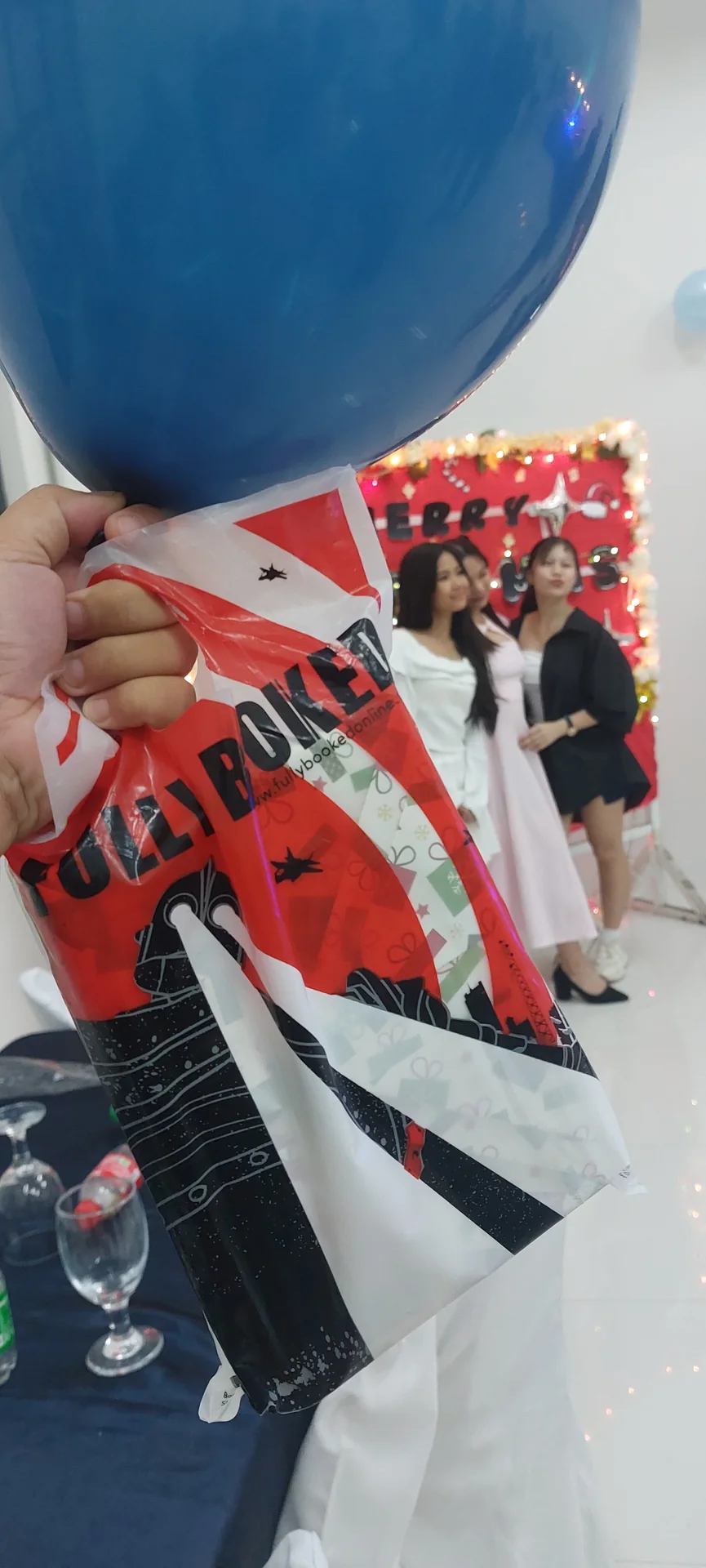 A wrapped Nancy Drew book held up at a Christmas gathering, friends celebrating in the background