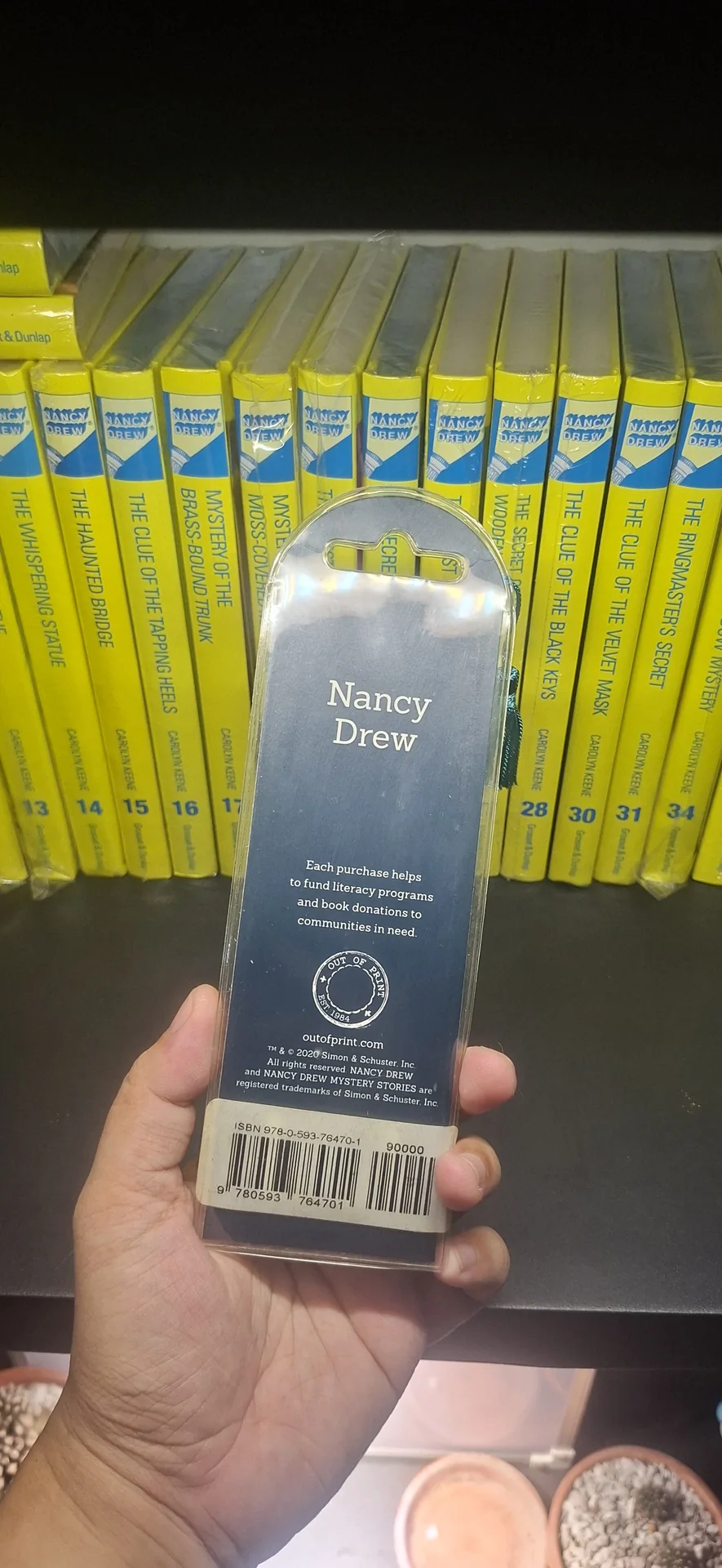 A Nancy Drew bookmark still in its packaging, held up in front of the shelf